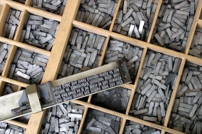 Un casier de bois compartiment&eacute;, rempli de caract&egrave;res d&rsquo;imprimerie en m&eacute;tal rang&eacute;s case par case ; au premier plan, une ligne d&eacute;j&agrave; compos&eacute;e attend d&rsquo;&ecirc;tre encr&eacute;e.